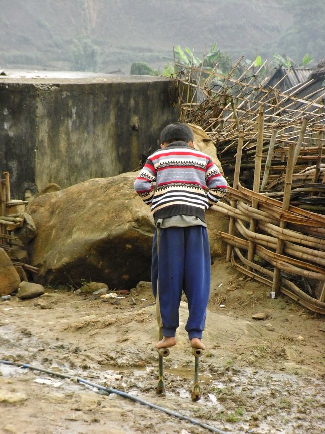 ぬかるみを竹馬で越えて行く少年。
