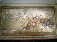 国立考古学博物館にはポンペイで発掘されたものを初め、古代ローマの遺物が大量に展示してあります。
中でも目玉はこの「アレクサンドロス大王とダレイオス３世の戦闘図」。イッソスの戦いを描いたモザイク画です。
個人の家の床のモザイクで、敵陣深く切り込んだアレクサンダー大王が、アケメネス朝ペルシャの王ダレイオス３世と至近距離で対峙している場面が描かれています。
紀元前３３３年に起きたイッソスの戦いは、ポンペイが埋没した紀元７９年から見れば４００年以上昔のはなしで、もはやアレクサンダー大王は伝説の英雄と化していたでしょう。現代人とあまり変わらない感覚で、この床のモザイクの絵柄を見ていたのだと思います。