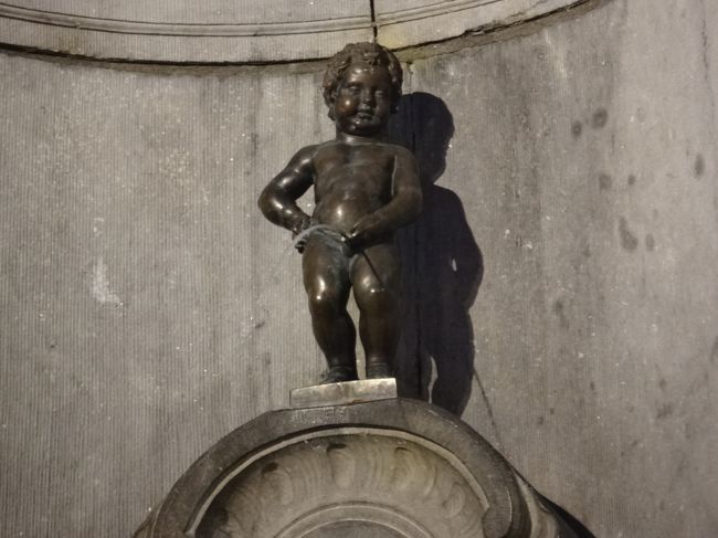 『小便小僧』（Manneken Pls）<br /><br />「ブリュッセルの最長老市民」のキャッチフレーズで<br />世界的に有名な「小便小僧」は、愛称「ジュリアン坊や」<br />（Le Petit Julien）としても親しまれています。<br /><br />「小便小僧」が製作された由来は、<br />幾つかあるようですが、<br />一つはブラバント公ゴドフロワ2世に関する説。<br />1142年に当時2歳のゴドフロワ2世率いる軍は、<br />グリムベルゲンでの戦いの際、戦場の兵士を<br />鼓舞するため、ゆりかごに幼い支配者を入れて<br />木に吊るした。<br />そこからブラバント公は敵軍に向かって小便をし、<br />味方軍を勝利に導いたというものです。<br /><br />また、一つは侵略者が城壁を爆破しようとしかけた<br />爆弾の導火線を小便をかけて消し、<br />町を救った少年がいたという武勇伝説。<br />この少年の名は、ジュリアン（Juliaanske）といい、<br />「小便小僧」の愛称はここに由来すると言われています。