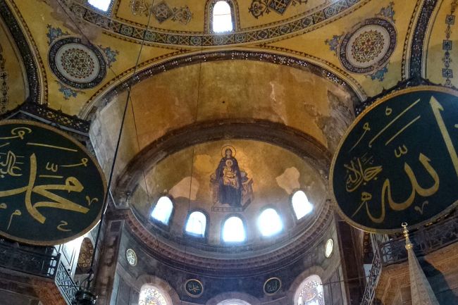 アヤソフィア上部には、アラビア文字でアッラーや預言者の名前が金のカリグラフィーで描かれた巨大な円盤が掲げられています。<br /><br />中央上部に描かれているのは「聖母子と大天使」