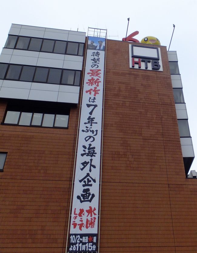 モエレ沼公園から走ること30分。<br />北海道テレビ/ＨＴＢに到着ですっ！垂れ幕で一気にテンションがアガる!!<br /><br />以下、しばらくどうでしょう藩士（水曜どうでしょうファン）にお付き合いください…。<br />深夜に録画した水どうを、夕食食べながら見るのが夫婦のささやかな楽しみでして(笑)ステッカーとかonちゃんグッズとか欲しかったんです。“聖地”にも行ってみたかったんです。運が良ければメンバーに会えるかなぁなんて。<br />だから、札幌へ行ったら絶対ＨＴＢへ行きたかったのですっ。