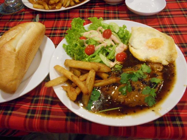 いただいたのは<br />・Banh My Bo Bit Tet<br />（バイン・ミー・ボー・ビット・テット）<br /><br />ボー・ビット・テットというのは牛肉のステーキのことです。<br /><br />ここで１０年越しで初めて知った真実！<br />バインミーって、サンドイッチのことじゃじゃなかったんだ〜。<br />パンのことをバインミーって言うらしくって、<br />わたしたちは、ステーキを挟んだサンドイッチが出るのかと思ったら<br />普通にステーキがお皿で出てきて、<br />そこのフランスパンが出てきた(笑)<br /><br />いやあ、何年経っても、新しく知ることってあるのね〜＾＾<br /><br /><br />それから、夕食用に２つテイクアウト<br />１つは、banh My Kep Thit Bo (サンドイッチ）<br />もう１つは　banh My Sot Vang(フランスパン付のビーフシチュー）<br /><br />これにレモンジュース２つで<br />369000VND（1680円）です。