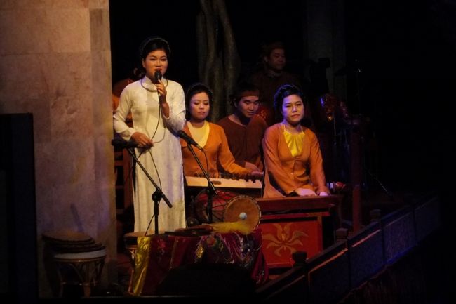 いよいよ開幕です。<br />まずは、伝統楽器による音楽が奏でられ、<br />そのあとに<br />きれいな民族衣装を着たお姉さんが<br />ベトナム語と英語で、簡単なごあいさつ。<br /><br />着ているのは、現代的なアオザイではなくて<br />古典的なアオザイのようです。<br />チャイナドレスのような上着がゆったりしてるのが<br />昔のアオザイのスタイルなんです。<br /><br />