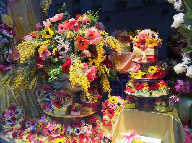 さて、ロックフェラーセンターのプロムナードに入りました。突き当りにはロックフェラーセンターが見えてます。<br />こちらのお花屋さんってほんときれいに飾ってる。<br />お花の需要がもしかして、すごいあるのかしら？