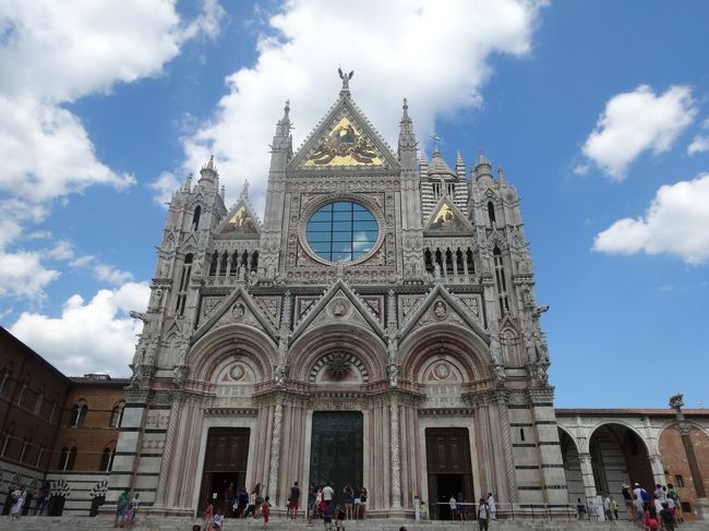 正面のファサードは、白と黒にさらに赤が加わり、金色のモザイクがトスカーナの強い太陽の光に輝き、まぶしい。<br /><br />14世紀末から、ずっ〜と、輝きつづけてきたのだろうか。