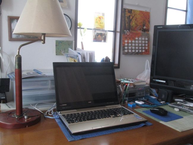 旅行のための調査や手配に使うパソコンが置かれた2階自室のテーブル。<br /><br />テーブルはマンション入居時に購入したダイニング・テーブルで150×84センチの6人用で十分広く、26インチのテレビと小物引出しも置いています。<br />パソコンは移動しやすく、傷つき防止のためランチョンマットを敷いています。<br /><br />無線LANではなく、1階リビングに置いたデスクトップPC用のルーターとLANケーブルでつないでいます。