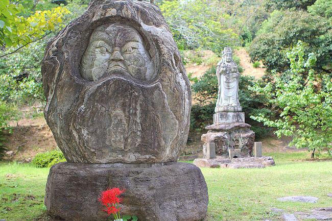ダルマ像に誰が供えたか彼岸花。彼岸花の赤が鮮やか。