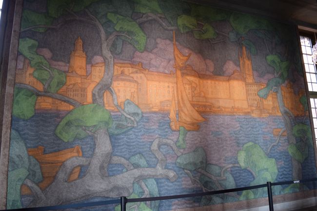 窓とは反対側には、壁にはフレスコ画が描かれていてメーラレン湖とストックホルムの街並みが描かれています。<br />当時のスウェーデン王国の皇太子ユーセン王子が5年をかけて描いたものらしい。。<br />この絵は窓から見える景色と同じものが描かれているらしく、窓がにいる方は景気が見えるが、窓を背に座っている方はその景色が見えないため、その方達にも素晴らしい景色が楽しめるようにと描かれたらしい。<br /><br />流行りの<br />"お・も・て・な・し"<br />の心ですね。<br />