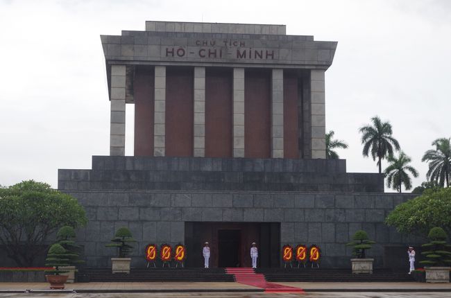 廟に至る通路で外国人観光客はひとまとめにされ、ある程度人数が揃うまで待たされる。ベトナム人はそこに荷物預け所があるので預けるが、外国人は持ったままでいいとのこと。その上でセキュリティチェックがあり、一眼レフのカメラは別のところに行き、カメラの絵が描かれた袋にカメラを入れ引換札を渡される。<br /><br />カメラを預けた人が揃ったところでいよいよ中へ。<br /><br />正面の扉から入り、階段を上がったところにいきなりホーチミンの顔がきている感じで、ややいきなり感で驚く。遺体はガラスケースに収められ、国旗や党旗などには包まれず、普通の青い中山服姿。<br /><br />そのすぐ脇に一段低く堀状になった所に不動の護衛兵が守護している。ご遺体だけかと思ったら兵士の顔が近くにあって驚く。左側のお顔近くから3辺をしずしずと進む。促されたわけではないのだが、止まってはいけないルール(あまりじっくり見られると色々困るからだと思うのだが)なので、ゆっくり歩きながら回る。<br /><br />独特の重苦しい雰囲気。お顔はお札などでよく見る顔そのままな感じがした。<br />これでレーニン、毛沢東、金日成、金正日と永久保存され展示されている世界の政治家を制覇した訳だが、一番生きているイメージに近いのはホーチミンかな？<br /><br />展示施設としても一番シンプルで、ご遺体の参拝？を終えるとすぐ階段で出口。<br />係員がカメラの絵が描かれた袋をこちら側に持ってきてくれて受け取る。