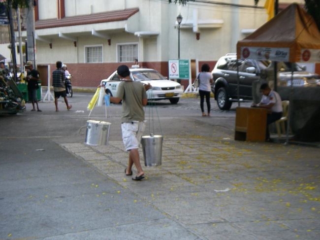 教会前の広場、駐車場で天秤棒を担ぐ人を見かけました。売っているのはジュース、水、何でしょうか？