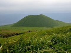 米塚。
草原に覆われたきれいな円錐形の丘だが、噴火口の後である。以前は頂上に登ることができたそうだが、今は登山は禁止されている。
むかし、阿蘇の神様が、収穫して積み上げたのが米塚で、あるとき阿蘇は大飢饉にみまわれ、人々は飢え死にしたり、草を食べたりしていた。阿蘇の神様は、これをかわいそうに思って、米塚の頂上の米をすくい取り、飢饉で苦しんでいる人達を救ったという民話があるそうだ。