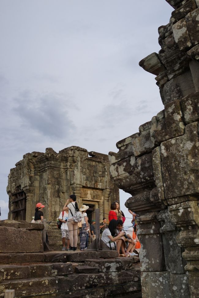 アンコール・ワットの次は、プノン・バケンでの夕日鑑賞。<br />プノン・バケンは丘の上にある遺跡で、頂上までは徒歩15分くらい。<br />日没は18時半頃との事だったけど、なぜか16時に麓から頂上へ向かう。<br /><br />早すぎでは？？と思ったけど、ここも入場制限があり、日没間際に行くと遺跡に登れなくなってしまうとの事。<br />確かに17時頃には遺跡の下に行列ができていて、登れなくなっていました。<br />夕方、ここに来る観光客は夕日目当ての人が多いはず。<br />だとすると日没までは下に降りないので、待っている人達は待ちぼうけだろうな。。。<br /><br />とはいえ、結局この日は夕方から雲行きが怪しくなり、夕日は観られませんでした。