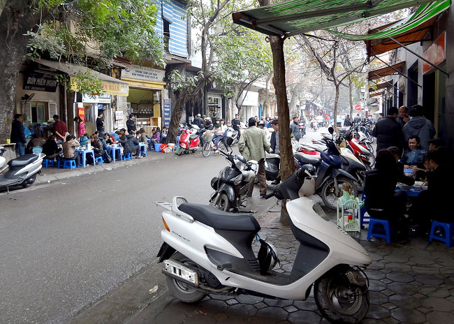 お昼時、歩道に並べられたおもちゃのようなテーブルで、例の低いイスに座って食事をとる人たち。