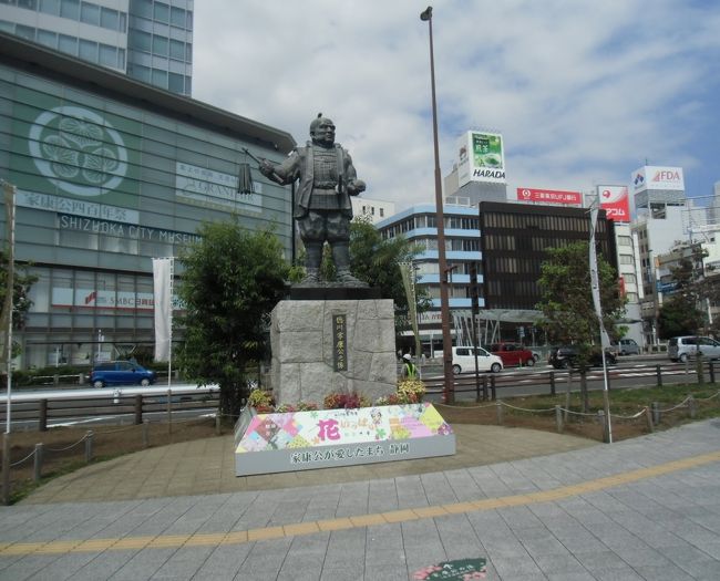 その北口のロータリーで 駅の方を向いて立つ家康<br />40代前半、天下統一間近の秀吉の家臣だった頃の像。<br /><br />背後（左）の建物（＝静岡市美術館）のガラスに<br />「家康公四百年祭」の文言と共に<br />徳川の三ツ葵の紋が描かれている。