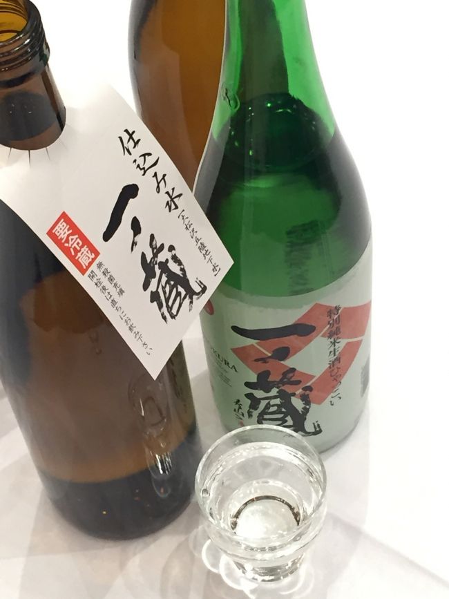 会場入り口で，グラスに入った一ノ蔵のお酒を<br />一人ずつ受け取ります．<br />お酒は，【ひゃっこい純米特別生酒】．<br />アルコール 15度．<br /><br />会場は18:15から入場でき，18:30スタートです．<br />少し時間があるのでアペリティフとして<br />『どうぞ』という趣向でしょう．<br /><br />会場内の丸テーブルには，<br />4合瓶の一ノ蔵が1本，仕込み水2本が置いてありました．<br />