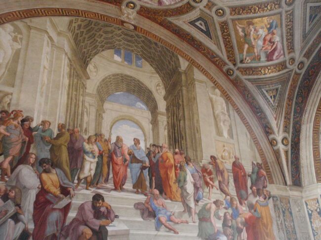 ラファエロ1509　「アテナイの学堂」　ラファエロの間<br />作品の中央左、天を指すプラトンは“レオナルド・ダ・ヴィンチ”、階段下に一人離れて肘をついて座るヘラクレイトスは“ミケランジェロ”、その右側に群衆の中でコンパスを持つユークリッドを“プラマンテ”、そして一番右側の人影からひとりこちらを見る男性には、ラファエッロ自身を登場させている。<br />◆フレスコ画で描かれた『アテネの学堂』は、半円形の画面に、だまし絵のようにアーチが続く神殿のような空間が描き込まれている。天井のタイルもアーチになった天井の一点に正確に収束する「中央一点消失法」の頂点といえる。