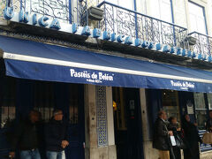 ネットで見たままのお店！
写真はカフェ利用後に撮影したもの。私が入るときはぜんぜん並んでなかった。
恐る恐る店内に入るとテイクアウト用のカウンターにスタッフが数人待機しているけれどお客さんはゼロ。
事前の口コミ調査で、天気が良かったらテイクアウトして隣のスタバでコーヒーを買って公園で、天気が悪かったら店内で、と決めていたのだけど席に座るのは少し勇気がいる…
思い切って奥に進むとカフェスペースがあり、何組かお客さんがいて少し安心。オシャレとは少し違うけど歴史ある感じの店内。作っているところが見られるスペースや幾つかフロアがあると口コミで見たけれど、一階が空いてるし勝手に行っていいのかわからず、大人しく一階の窓際に着席。
メニューをもらって、ナタを何個頼むか悩む。小さいから三個くらいは食べられるという口コミを見たけれど、甘くて飽きるかもと思ったので結局二個注文。コーヒーはかなりの種類があってよくわからなかったけれど、ポルトガルでは普通にコーヒーを頼むとエスプレッソが出てくると聞いていたのでカプチーノを注文。