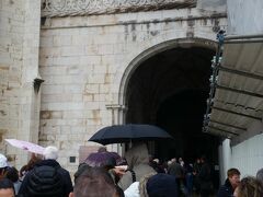 ジェロニモス修道院は人気スポットで並ぶので、先にベレムの塔に行ってチケットを発券してもらったほうが良いらしい。でも朝一なら大丈夫かもと思って先にジェロニモス修道院へ。
しかし、やはり皆考えることは同じで１５分程前に到着したけど既にたくさんの人がチケット売場が開くのを待っていた。
念のため前の方に行って行列の先を確認。列は二つできていて、一つは有名な回廊を見ることのできる有料の入口、もう一つは無料で入れる教会の入り口にできていた。ほとんどの人は有料の方に並んでいて、私はリスボンカードがあるので無料で入れるけれど発券が必要なので同じ列に並んで待つことに。
雨がパラついていたので傘売りのおじさんや、物売りのおばさんが列の間を行ったり来たりしていた。
１０時になって入口が開くと列は動きだし、前にいた団体客が間違えて教会の入り口の方に流れたようで結構人数が減ってラッキー！

しばらくすると列の途中で誰も並んでいない場所にチケット売場らしき場所がある。奥を覗いてみるとカウンターにスタッフが座っていてチケットを買えそうな雰囲気。
ポルトガル語でチケット売場のような表示があって、前に並ぶ観光客だたちはヨーロッパ系のようだから言葉読めそうだけど誰も見向きもしないし、スタッフも並んでいる人たちを見ても何も声かけしていないし違うのかなぁ、とモヤモヤ。
こういうとき連れがいたら並んでてもらって聞きに行けるんだけど…
結局もし違ったときにまた並びなおさなきゃいけなくなったら馬鹿らしいのでそのまま並んで待つことに。でも気になってその場所を見ていると、別の観光客が立っている警備員らしきおじさんに聞きに行った！
何を言っているかわからないけど、身振り手振りから「ここでチケット買えるの？」「買えるよ」「じゃあどうしてみんな並んでいるの？」「さあね」みたいなやり取りみたい…。その後その観光客はそこでチケットを買ったみたいで、私のずっと後ろにさっきまで並んでいたのに、横をスーっと通って先に中に入っていった…
やっぱりあそこで買えたんだ！と思ったけどもう間もなく自分の番だったので結局そのまま並んでチケットを発券してもらった。
警備のおじさんもチケット売場のおばさんも、そこで買えるなら教えてよ〜。