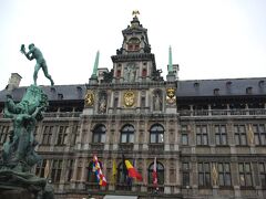 市庁舎です。先ほどの出っ張った建物は市庁舎の横っ腹でした。
１５６５年完成のルネッサンス様式。手前の旗は、左からアントウェルペン州・ベルギー・基礎自治体（日本の市のようなもの）です。
青銅の「ブラボーの噴水」が目を引きます。
ブラボーは古代ローマの兵士で、この地域で狼藉を働く巨人アンティゴーンの手を切り落として、川に投げ捨てました。
「手を投げる」という言葉が町の名前の由来だとする説があり、その象徴としてこの像が建てられました。
アントワープは、Ａ．Ｄ．２世紀頃からの歴史を持ち、１６世紀には国際貿易の中心地として発展しました。
しかし、１５８５年にスペインに占領され、多くの商人であるプロテスタントが隣国オランダに移住し、世界の商業・金融の中心はオランダに移って行きました。
アントワープからオランダ国境までは、わずか30ｋｍです。
