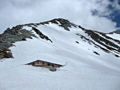 室堂山荘（標高約2400ｍ）から一ノ越山荘（標高約2700ｍ）までのコースタイムは1時間半。
しかし、ソレはグリーンシーズンの話で、雪が積もるこの時期はもう少し長く、2時間弱かかってしまった。

室堂山荘の前には小さな小屋（写真）があるのだが、その小屋はほぼ屋根の高さまで雪に埋もれ、かろうじて三角屋根が見える程度だ。
そして、その後ろに見える山が、これから登る山：雄山だ。

立山のゴールデンウィークは、どう見ても未だ冬だ。
