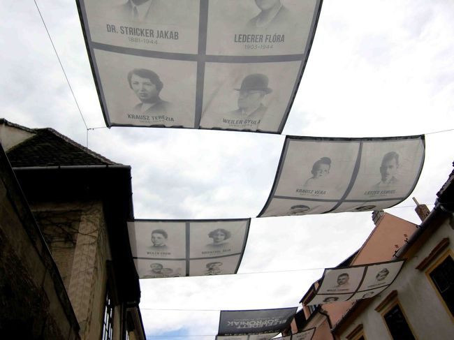 上を見ると、布の幕が凧のように揺れています。そこには人物の写真が。<br /><br />ショプロンに住んでいたユダヤ人で、アウシュヴィッツなどに送られホロコーストで亡くなった方々の写真です。<br />