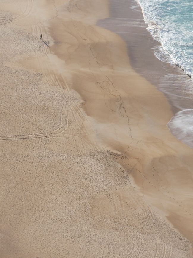 左上に黒点がみえる。これは、浜辺を散歩する人と人の影です。