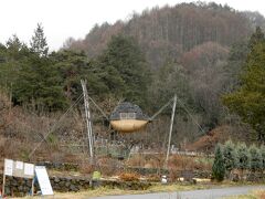 緩やかな坂道をユルユル登っていくと、前方に奇妙な物体が宙に浮いているのが見えた。
農家が立てた害鳥避けかとも思ったが、それにしては形状が珍妙過ぎる。
手持ちの観光案内地図で調べてみると「空飛ぶ泥舟」という茶室だった。
茅野市出身の建築家、藤森照信先生の設計によるもの。
2011年に茅野市美術館で開催された藤森照信展に展示された後、ここに移築されたという。
なお、空飛ぶ泥舟は藤森先生の所有なので、イベント等を除き建物内部への立ち入りは不可。
外から見上げるしかない。