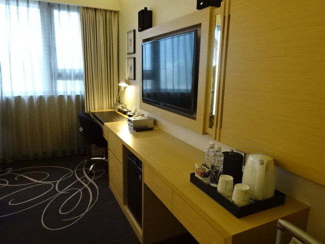 ベットの向いにはデスクとテレビ。無料のお茶類などが。お茶の前にある空きスペースにトランクケースを置くことができます。