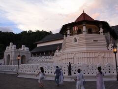 １８時１５分、プージャーの儀式が３０分から予定されている仏歯寺へ。

白亜の外壁が薄れゆく夕日に照らされてほのかにオレンジに染まり、優美な印象を醸し出しています。

その手前にはプージャーの儀式に出席しようと道を急ぐ、白い衣装に身を包んだ信者たちの姿が。