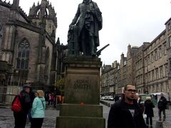 写真は聖ジャイルズ大聖堂の前に立つ経済論「国富論」の
アダムスミス像です。
学生時代に経済学を学んだものとしてまずは「経済学の父」に
詣でました。
（しかし勉強を一生懸命しなかったことが今でも悔やまれます）

昨日（9月15日）はヒースロー空港到着後、空港近くにあるibsロンドン・
ヒースローエアポートに宿泊しました。
先回の世界一周旅行(2015年3月）の際に利用したホテルであり
空港からのバスを問題なく利用してホテルにチェックインできました。
翌日はホテルからまだ朝の暗い中、6時半ごろのバスを利用し、9：05
ヒースロー空港出発のBA便でエディンバラ空港に向かい10：40に
到着いたしました。
空港に到着後インフォメーションセンターでエディンバラの中心部まで
バスで行くべきかトラムで行くべきかをスタッフの方に聞いてみることに
しました。
以下はそのやりとりの内容です。
スタッフは私より少し年下の方で好感が持てる女性でした。
「中心部に行くのにバスとトラムとどちらが良いですかね。」
「どこまで行かれるのですか。」
（地図を示しながら）「このYMCAまでです。」
「私だったらトラムを使うわ。終点まで乗り換えなしで行けるし、
YMCAは終点駅のYork Placeから歩いて5分くらいよ」
「そうですか。私は44年前22歳の時エディンバラに来たことがある
のですが、ずいぶん様子も変わってしまったのでしょうね。」
「いいえ、エディンバラはあなたが青春時代に来た時と少しも
変わっていないわ。
いまでも"Good and old days"のままよ。」とのこと。
「スコットランド人のホスピタリティも変わっていないようですね。
今回は家内にスコットランドの素晴らしさを見せてあげたいと思って
再訪したのです。」、「ところで今日のお天気はどうですか」と
聞いてみた。
すると横で私たちのやり取りを聞いていた、これも同年代の女性スタッフ
が突然廊下に出て額に手をかざしながら窓の外の空を見上げて。
「今のところは大丈夫みたい。雨は降っていないわ。」とのこと。
私はてっきりPCかスマホで天気予報を調べて教えてくれると思っていた
のですが予想外のアナクロですが温かい対応で天気予報をしていただく
ことが出来ました。
PCもスマホも携帯もないアナクロ時代に旅をしていた私にとって
人間的な懐かしい対応をして頂きました。
人間から得る情報は肌の温もりがして心が温かくなりました。
何気ないやりとりでしたが心が通い合うような場面を頂いて
今回の旅も楽しくなるような気がしてきました。
良い出逢いは良い旅のリトマス試験紙です。
私たちは早速空港前のトラム駅の自販機でチケットを購入し
終点駅のYork Placeにむかいます。
自販機はカードを利用しましたが画面に表示される指示に従って
行えば問題なくチケットが出てきました。
でも実際は初めてですので慣れないのであわててしまい
上手に操作ができないので家内に案内表示を読んでもらいながら
操作を行いました。
これで二人の旅のチームワークの必要性を改めて認識いたしました。


