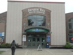 シャーロットタウンのインフォメーションセンター
がある「Founders Hall」の正面です。
港が近い通りにありました。
2台のパソコンがあって日本語バージョンでも
使用できました。
入口すぐ左にグレイハウンドのツアー会社があり
ここで「赤毛のアンツアー」を申し込みました。
グレイハウンドの「赤毛のアンツアー」は
ホテルから受付嬢にお願いして
電話で事前予約
として申し込んでいました。
カードで支払い、
一人で約75カナダドル（税込）
2人で約150カナダドル（税込）で日本円に換算
しますと合計13,513円でした。
観光の当日（10月1日）に受付カウンターでアジア系の
美しい女性の方にバウチャーを見せると
「日本人の方ですか？クルーズですか？」と
聞かれました。
その方は日本人の方で
シャーロットタウンに20年以上住んで
いらっしゃるということでした。
受付カウンターの右に
カフェとその奥にトイレがあります。
ホール前の道に観光用の大型の
白いバスが停まっていました。
もうバスの受付が始まっていましたので
私たちはも列に並びました。
私たちの前にならんでいた
同じ年齢位の白人ご夫婦はロンドンから
やってきた観光客の方でした。
ご主人に「どちらの方ですか？」と尋ねられたので
「日本人です。観光でイギリスのスコットランド、スカイ島、
湖水地方、コッウォルズ地方、ロンドンを観光して、
昨日、シャーロットタウンに来ました。」と
説明しました。
「私たちイギリス人もそんなに多くの所を
観光したことがありません。
ところでロンドンは気に入りましたか？」と
質問されました。
「私たち夫婦はとても気にいっています。
歴史のある都市ですし。
観光どころもたくさんあります。
特に博物館が素晴らしいですね。
あれだけ多くの
また価値のある展示物を見ることが出来て、
かつ無料であるということに感動しました。
それに天気も雨もなく
暖かくて良かったですしね。」
と返答しますと
「最近はロンドンのことを
よく言わない人も多くいて
いまのご意見を聞いてうれしいです。」
とのことでした。
きっとテロ事件やEU離脱のことを
気にされていたのかもしれません。
「私は44年前の青春時代に
ロンドンで英語の勉強をいたしました。
ロンドンは私の古き良き青春時代の
思い出がたくさんあります。」と
言いますとご主人は喜んでいました。
イギリスを観光した時、
期待していた以上にイギリス人が親切であった
ことを思い出しました。
「色々大変な事件が起きているときに、
私たちの国によく観光に
来てくれたなあ。」という
気持ちがあって親切にしてくれたのかも
しれません。
それとも
「こんなに年を取っているのに
遠い日本から個人旅行でがんばっているなあ。」
と思って優しくしくれたのかな？
どちらにしても親切に扱われたことに
感謝したいです。

しばらくすると列の後ろから
同じバスに乗る観光客がどんどん
増えててきました。
「え～！インフォメーションセンターの中に
こんなに大勢の
人たちが待っていたっけ？」と驚きました。
後で知ったことですが
シャーロットタウンの港に
大きなクルーズ船が接岸して、
その船からの観光客が
ドット到着したことが分かりました。
クルーズの観光客の方に聞いたのですが
このクルーズはニューヨーク発で
プリンスエドワード島経由
ケベック行きのクルーズでした。
この豪華客船とはケベックの旧市街の港で
偶然に再会することになります。

バスの運転手さんの名前はジョンさん、
観光ガイドのおばちゃんはウェンさんでした。
二人名前を合わせますとジョンウェンですので
覚えやすかったです。

バスの中に入って座席に座っていますと、
道の向こうからアジア系の
小柄な若い女性が
キャリーバッグを引きながら歩いてきました。
インフォメーションセンターに入って
手ぶらで出てきたので
受付カウンターなどで
荷物を預かってくれるということが分かりました。
バスの私たちの後ろの席に一人で座っていました。
この方との楽しいエピソードは後述いたします。