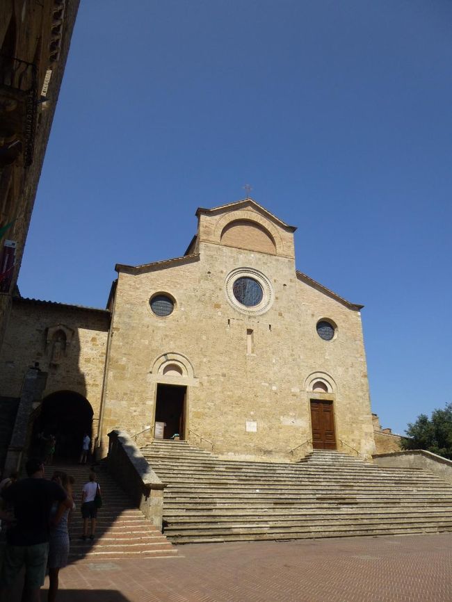 Collegiata di Santa Maria Assunta /Duomo<br />参事会教会 /ドゥオモ<br /><br />12世紀、ロマネスク様式<br />被昇天の聖母マリアに献堂<br /><br />浅い段差の階段アプローチ、その先に建つシンプルで美しいファサード<br />けどなかなか日陰から足が踏み出せな～い<br />意を決して中へ<br /><br />堂内（入場料 4eur。写真撮影×）には、矢が刺さりまくりの Bennozzo Gozzoli ゴッツォリ「聖セバスティアヌスの殉教」（1465年）、Domenico Ghirlandaio ギルランダイオ、Lippo Memmi リッポ・メンミなど錚々たる面々による作品群<br />最後、目に飛び込んでくるのは頭上の壁を覆いつくす地獄絵図<br />Taddeo di Bartolo「最後の審判」（1393年）<br />画のタッチの好き嫌いはさておき、目を背けたくなる生々しい光景なのに隅々まで追わずにいられない。何かに「人は、死によって何より生を体験できる」と書いてあったけど・・・そういうこと、なのかな<br /><br />一番「いい」印象に残ったのは、素朴で心地よく暖か～い木彫の大天使ガブリエルとマリア像。なんとルッカのDuomoでみた美しい石棺を手掛けたヤコポ・デッラ・クエルチャの作品！全然っ違う感じ。こっちの方が好き！