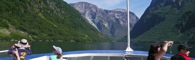 海抜1800mの岩盤を滑り落ちる滝があるかと思えば、苔の群生化とも見えるやわらかい岩肌。<br /><br />真夏なのに残雪が残る頂。<br /><br />雄大な風景につい普通の山岳渓谷と錯覚してしまい、船べりの先端で身を乗り出している女の子が振り落とされないか気をもんだが、ここは海抜０ｍ。<br /><br />鏡の様に滑らかな水面を、船は滑るように進む。<br /><br />写真はその中を何とか陣取った遊覧船の帆先からのもの。