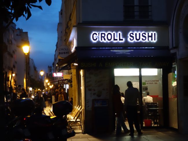 寿司屋。暗くなっても人通りは絶えず，食事している人多数。