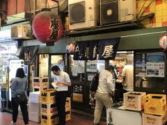 決めた店はここ。
環状線の高架のところにある「銀座屋」。
満員で入りずらいうえ、喫煙と禁煙で入り口が分かれている。
コの字のカウンターで立ち飲み式。
愛想のいいお姉さんが１人で手際良く回しており、少し待ったが店内に案内してくれた。