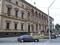 「旧財務省ビル」に着きました。1858-62年に建設され、財務省ビルとして使用されていましたが、現在はメルボルン博物館として無料で公開されています。建物内部も美しく、展示物も見応えがあります。特に、住込みの管理人が８人の子供たちと生活をしていた地下部分は興味深い展示でした。ただ、中国人の家族連れがたくさんいらして、声高に喋り、狭い館内でポーズを取って写真を撮りまくるのには閉口させられました。
ちなみに写真の車横を歩く黄色いベストを着た男性2人組は、隣のビルの修理をしている建築作業員です。これがこちらでは制服のようです。彼らも何故かショートパンツ姿。