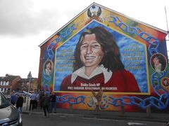 Bobby Sands Mural
フォールズロードに来ました。
ここは各観光ツアーには欠かせない場所なのでこの時も次々と
観光客が来ては写真を撮っていました。

Sinn Fein
ちなみにこのミューラルがある建物にはシン・フェイン党のおみや店が
あるのでそこにも行ってみました。
中には様々なグッズが並ぶ中、私が欲しかったケルト十字のピアスが
あったので購入しました。
ここの店は他店と1ヶ所異なる点があって、店を出る時は店員さんに
一声かけて鍵を解除してもらわないと外に出られないことです。
今でも用心のため、施錠しているんでしょうね。