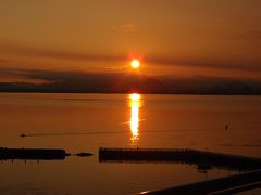 朝、目が覚めたら窓のカーテンが赤く染まっていたのであわてて開けて撮影。
日の出時刻から15分ほど過ぎた琵琶湖、朝日の下を横切るように小さな船が進んでいました。
背景に雲があり見えづらいですが、太陽の右下に見えるシルエットは近江富士（三上山）です。