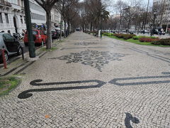 リベルダーデ（ポルトガル語で自由）大通り
１７５５年大地震の後、都市再生計画によって造られた幅９０m、長さ１５００mのリスボンを代表する通りです。綺麗なモザイクの歩道が続く繁華街です。
雨が随分降ってきました。雨に濡れてモザイク模様がクッキリと見えます。
プラタナスの植え込みのある綺麗な道を南へ歩いて行きます。天気が良いと散歩には最適です。