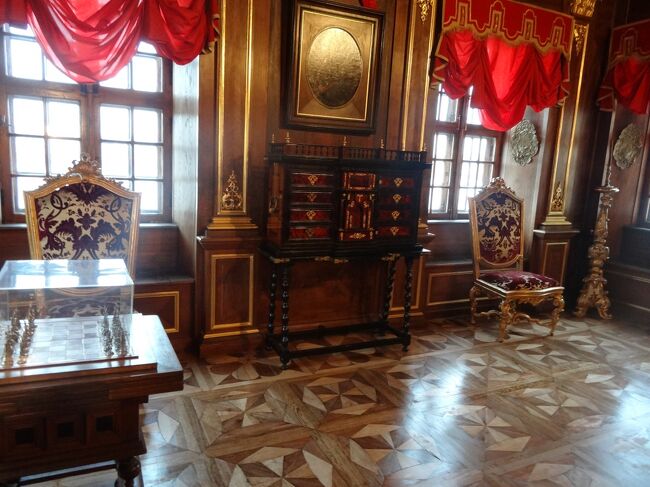 ピョートル1世の肖像画が飾ってあるWalnut Study(17)です。<br />光っちゃってどうしようもないです。<br /><br />G.フォンタナ《1670-?》, J.シェデル《1680-1752》<br />メンシコフ邸　クルミ材の書斎　1717<br />メンシコフ邸の設計図の作成者は未だに確定されていないが、1703年にイタリアからロシアに出仕したジョバンニ・フォンタナだという説が最も優勢である。邸内各室はどれも明るく広々としていて、いくつか縦列に縮まっている。ピョートル時代の例に漏れず内装は豪華で、デルフト陶器のタイルや高価な南洋木材が多用されている。このクルミ材の書斎は修復を終えている部屋の中の精華であり、壁を飾る木彫りの羽根板の暖かい色合いに金鍍金の文様装飾が美しく映える。極めて保存状態の良い天井画にはピョートル一世が古代神の姿で描かれている。書斎の内装の仕上げともいえるのが、部屋の隅のデルフト陶器製タイルで覆われたペチカだ。（土産本）