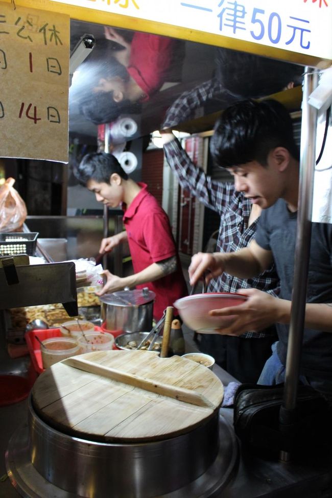 数少ないテーブルで食べている人の料理を眺めていると<br /><br />「おでん&amp;麺」の組み合わせばかりだ。<br /><br />「甘いモツ」はどれだ？？<br /><br /><br />結局よくわからないので、前に並んでいる人に聞いてみる。<br /><br />夫婦とおばあさんの３人組。夫婦の年は僕と同じくらい。<br /><br /><br />台湾の人はみんな親切なので、質問することにためらうこともない。<br /><br />「すみません。ここではどんな風に頼むんですか？」<br /><br />すると、3人とも、好意的な表情で僕を迎えてくれる。<br /><br />旦那の方が<br />「麺と天ぷらをセットで頼むのがいいよ」という。<br /><br />妻の方も<br />「そう。見てごらんないよ。みんな、麺と天ぷらを頼んでるわ」<br /><br />天ぷら？？<br /><br />どーゆーこっちゃ？？<br /><br />誰も天ぷらなんて食べてないよ？？<br /><br /><br />一度頭にクエスチョンが浮かんでしまうと、<br />今の僕のレベルでは<br />早口でまくしたてるネイティヴ中国についていくのは不可能だ。<br /><br />話し終わったところで改めて聞いてみる。<br /><br />「というと、ここのメニューは何々あるんですか？」<br /><br />一通り説明した後に、スタートに戻る質問をされても、<br />彼らは嫌な顔一つしない。<br /><br />「いやだから、『大腸麺線』と『天ぷら』だよ」<br /><br />「天ぷら？？」<br /><br />「あなた日本人なのに、天ぷら知らないの？」<br /><br />？？？<br /><br />天ぷら？？<br /><br />どこにも書いてないじゃん…<br /><br />つーか、誰も食べてなくね？？<br /><br />…<br /><br />…<br /><br />あっ！！<br /><br />わかった！！<br /><br />甜不辣！！<br /><br />甜不辣（ティエンブーラー）<br /><br />甜（てん）不（ぷ）辣（ら）！！<br /><br />わかった。<br /><br />やっとわかったよ！！<br /><br />当て字なんだね！！<br /><br />あのおでんと思ってたの、天ぷらか！！<br /><br />僕は<br />「明白了（わかったよ）！！」を繰り返す。<br /><br />辛抱強く説明してくれた夫婦は、「ようやくわかってくれたか??」と明るい表情になる。<br /><br />そして彼らは、恐らく２回目となる説明を繰り返してくれた。<br /><br />要はメニューは<br />「大腸麺線」と「甜不辣（天ぷら）」の２種類ということらしい。<br /><br />で、どちらも50元≒200円。<br /><br />「大腸麺線」の辛さはお好み。<br /><br /><br />「それでお腹いっぱいなる？」と聞くと<br /><br />「バッチリだ」という。<br /><br />そこに奥さんが<br />「ここの唐辛子はものすごく辛いから、私は〝微辛〟にしているわ」と、<br />これまた常連らしいアドバイスをくれる。<br /><br />〝微辛〟<br /><br />初めて聞く表現だ。<br /><br />台湾中国語らしい、優しい響きだ。<br /><br />この短時間で、新単語２つも習得した。<br /><br />僕も<br />「辛いのは苦手なので、〝微辛〟のにしよう」とさっそく新単語を使ってみる。<br /><br />痔持ちなので、辛いのは避けたい。<br /><br />僕の番になって<br />旦那さんが「彼の分も頼んであげなよ」というと<br /><br />店の主人の近くにいた奥さんが<br />「彼も天ぷらと大腸麺線を微辛で一つずつ」と頼んでくれた。<br /><br />ありがとう。どうもご親切に。