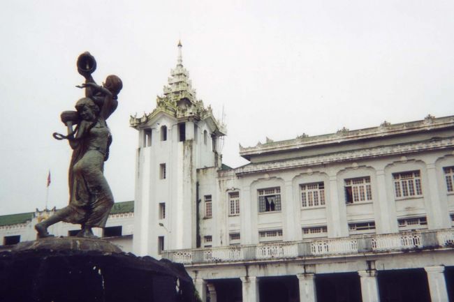 ■６日目(7/27）<br /><br />朝、下痢。ガイドブックには「下痢はミャンマーへの通過儀礼など」と書いてあったので、「とうとう私もミャンマーに受け入れられたんだ。」と軽く思い、臆することなく観光に出発した。<br />今日はティーダを伴ってヤンゴン鉄道に乗る。どこへ行くというのではなく環状線に乗り、人々をウォッチングし、３時間程度汽車に揺られヤンゴン駅にもどるという趣向だ。運賃は７チャットなのだがけれど外国人は1＄だった。パスポートの提示も要求される。現地の人はフリーだが有名バゴダの入場も５＄。そうして外貨をかせいでいる。<br /> <br />きちんとしたインフォメーションがあるわけでなく、電光掲示板があるわけでない。ホーム移動も線路に降りて行った。足下をみれば、色々と厄介なものが落ちている。踏まないように注意深く歩いた。<br />乗車した環状線の列車には木製の座席が、横一列に窓際に着いている。レールの整備が不良のせいか、少し横に滑る時もある。他の乗客が奇異な目で私を見る。庶民の足であるローカル路線に外国人が乗っている・・というのは確かに珍しいことかもしれない。回ってきた車掌は、身の安全のために警備の兵士がいる客車に移らないかと勧めてくれた。が、移動のためではく、ここに住む人たちの姿をウオッチングするのが目的だったので、このままいることにした。<br />車窓に広がる光景は、ビーンズ畑や外観がみすぼらしい何かの工場が目に入ってくる程度で、これと言った特徴的なものはなかった。トイレ事情を反映して、線路際の草むらにしゃがむこみ用を足す男たちも時々見かけた。<br /><br />※駅前<br />