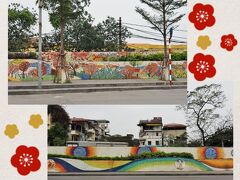 14:40頃、ロンビエン・バスターミナルに戻ってきました。なかなか来ないバスを待つ時間が長くなってしまったため、ちょっと予定が押しているような気もするけれど・・・ここに必ず行かなくては！というほどのものはないため、今からいわゆる・・・インスタ映えスポットを巡ってみようと思います。

バスを降りると・・・広い道路の東側には、住宅地と隔てるモザイク壁画が何㎞にもわたって続いています。昨日タクシーからも見ましたが、十数mごとに絵柄のデザインが異なります。モザイク壁画は、バッチャン村の陶器で出来ています。