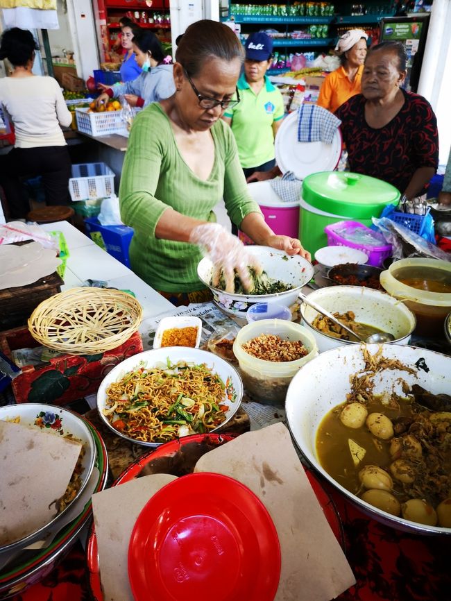 ある日の朝食は鶏肉おかず乗せ粥（ブブルアヤム）<br />これもなんと、１人前は5000Rp！<br />シンドゥ市場には場内外にブブル（ナシチャンプル）屋さんが出店してます。<br />中でも一番ラメィ（人気がある、混雑している）なオバちゃんが<br />まさにこのおばちゃん！<br />サヌールで聞けば誰でも知ってます。「ああぁ、市場の角の店の！」