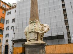 ［12:58］
【遺跡No.37】ミネルバ・オベリスク
パンテオンの南東にミネルバ広場があります。
その中央には可愛らしい象の彫刻があり、ミネルヴァのひよこと呼ばれています。これもベルニーニの作です。
そして象の背中にはオベリスクが乗っています。１世紀末頃にエジプトから運ばれてイシス神殿に建てられていたものです。
そのエジプトの女神イシスを祀るイシス神殿は、この広場の東にありました。これまでに見たナヴォーナ広場のものやパンテオン前のものも建っていたところです。今はサンタ・マリア・ソープラ・ミネルヴァ聖堂という教会が建っています。後ろの修復中のものがその教会です。