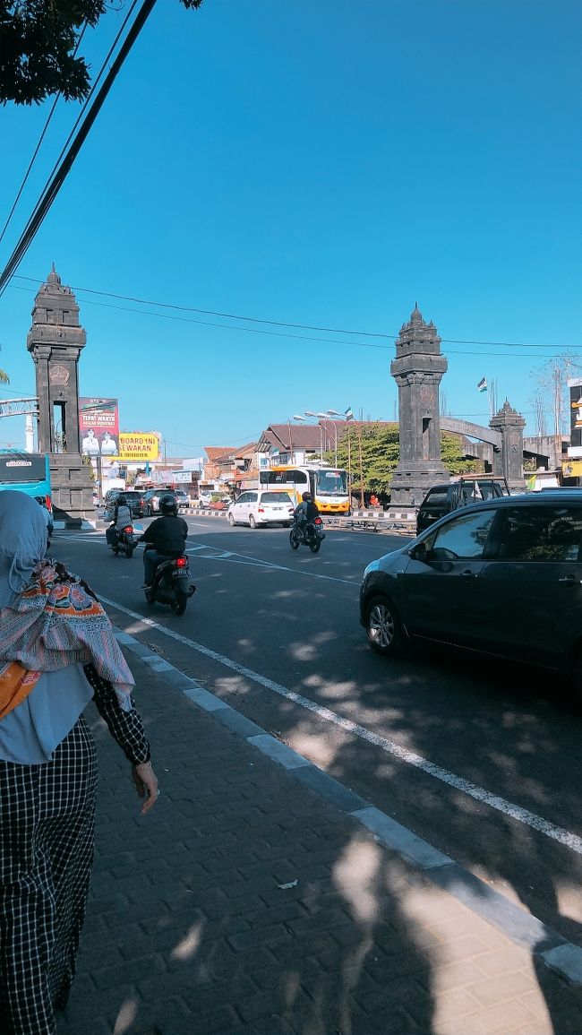 バス停で待っているとインドネシア人のおじさんに声をかけられました。どうやら彼もプランバナンに行くようです。話をしていると、彼の息子は埼玉で2年間留学をしたことがあるようで、日本に詳しい方でした。<br />１Aのバスに乗って少しすると、全員降りるように言われました。おじさんいわく、バスの調子が悪いので代替便で行くということでした。（英語のアナウンスがないので助かりました・・・）<br />道も混雑しており、プランバナンのバス停まで１時間かかりました。時刻は15時過ぎ。おじさんが寺院まで案内してくれました。<br />バスを降りたら大通りを渡って右に歩いて行きます。駐車場の入り口の脇から史跡公園内へ入っていきました。<br />写真はバス停から寺院までの途中のものです。