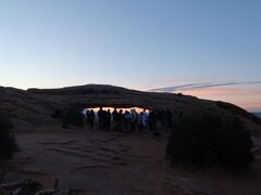 メサアーチ Mesa Arch
駐車場に到着する頃には、うっすら明るくなってきました。
車はけっこう止まっていました。トレイルをかなり急ぎ足で歩きます。
メサアーチが見えました。アーチ前には人が集まっています。