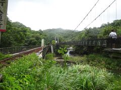 　11:30、十分は狭いエリアで集合場所もすぐ近くであったためか皆さん時間通り集まっており、バスも直ぐに来て十分大瀑布へ。十分駅から十分大瀑布へは歩けば約25分ですが、バスは乗って約6分の所にあるShifen Waterfall 停留所手前に降り、十分大瀑布まで約400ｍ歩きます。バスを降りた地点は十分街から約1.1Kmはあるので約15分ほど楽でした。
　途中には平渓線の線路と平行する「観瀑吊橋」があり、橋を渡っている時に運良く列車が通れば、皆さん手を振ってくれます。