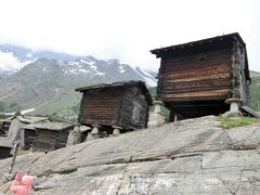 村の駐車場に到着しました。村は標高1798mの高地にある山岳リゾート地。ツェルマットと同じく環境保全のため一般車両は侵入できず村内では電気自動車のみが走っています。
駐車場でバスを降り、10mほど歩いた時でした。何やら冷たいものがポツリポツリと空から落ちてきたではありませんか。
「えっ、雨？なんで、さっきまで天気良かったのに。」、地面のコンクリートには雨の雫の跡が増えていきました。
「すみませーん、傘取ってきます。」と添乗員に告げて私はバスの中へ。
私だけでなくほぼ全員が雨具を持って再び集合しサースフェーの観光開始。
駐車場から続く坂道を下っていくと道の両側に古めいた木造の小さな小屋がいくつも見えてきました。
これはスイスの山村に昔からある木造の倉庫です。冬の寒さに耐え得るように分厚い木造の板で作られていて、寒さを凌ぐために窓は南側に一つしかありません。
建物は高床式になっていました。