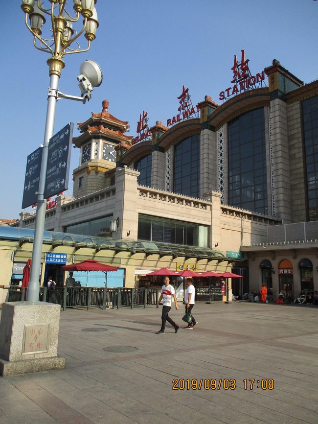 ↑ 北京駅。<br />　北京駅東街沿いにしばらくゆくと、風雪を感じる北京駅が現れる。<br />　いまの駅は建国10年目に前門近くから移ってきたはずなので、まだ60年しか経ていない。<br />　駅舎の通路の日陰では荷物を抱えて座りこんだり、ごろりと寝そべっているひとたちで溢れている。ひと昔前の日本の駅もこんなふうだったかな。<br />　さて、切符売場への入り口の手荷物検査場。<br />　外から見えるように持っていたペットボトルを女性の検査員に指さされた。<br />　まずかったかな？　<br />　と思っていると、「その中身を一口飲め」と言われたので、状況がわからないままゴクリ。・・・何ともない。<br />　これでようやく中身が危険品でないことを証明できたせいか、水入りボトルはそのまま持ち込めた。<br />　予約しておいた３日後の ”北京南→瀋陽” の列車の切符（紙質票）は、乗車駅ではないここ北京駅で入手できた。